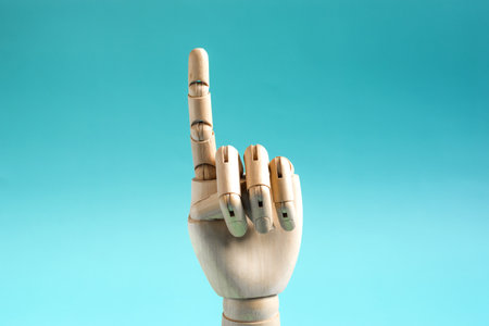 A wooden hand with a raised index finger on a blue background. Conceptual gesture in attention or stopの写真素材