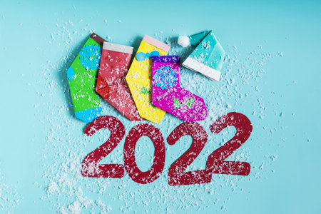 Bright Christmas decor, colored socks, a Christmas hat and the numbers 2022 in artificial snow on a colored background.の写真素材