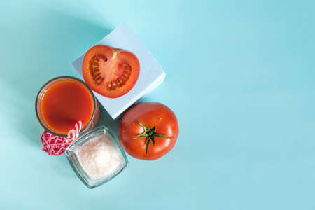 Flatley fresh tomato juice in a transparent glass with a decor of tomatoes and salt on a blue background of copy spaceの写真素材