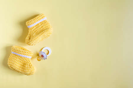 Flatley on the subject of things for the baby. Children's knitted shoes and baby pacifier on a yellow backgroundの写真素材