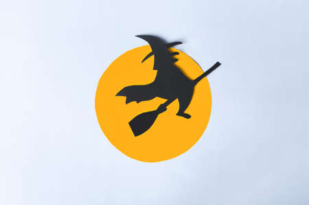 The shadow of a black ghost in a hat on a broomstick against the background of the orange moon disk close-up.の写真素材