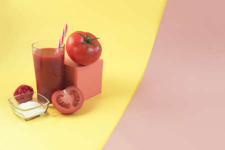 Tomato juice in transparent dishes and decor made of tomatoes, red cubes and salt on a yellow-pink background copy spaceの写真素材