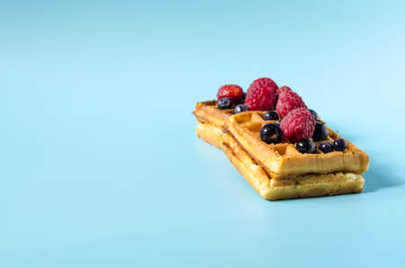 Baking fresh waffles with black and red berries on a blue background of hard light. Homemade cakes crispy waffles on a colored backgroundの写真素材
