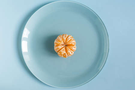 Concept bright peeled tangerine on a large blue plate on a blue background close-upの写真素材
