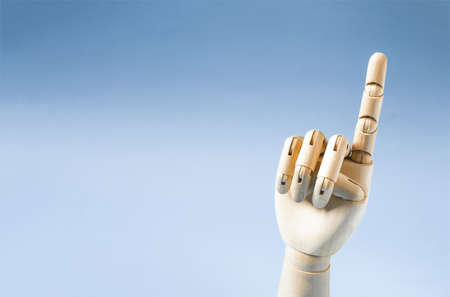A wooden hand with a raised index finger on a blue background is a place for text. Conceptual gesture attentionの写真素材