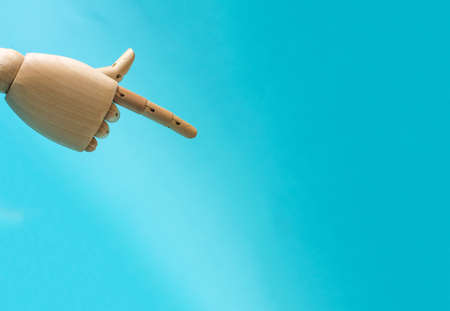 Wooden hand with outstretched finger pointing to a lot of empty space bright blue backgroundの写真素材