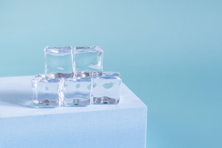 Transparent ice cubes on a blue podium and a light background of kopi space. Background of transparent ice cubes close-up and.の写真素材