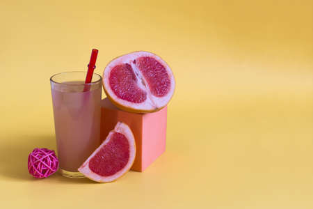 Grapefruit juice and grapefruit slices on a yellow background. Grapefruit juice in a glass glass with a red tube on a yellow background place for textの写真素材