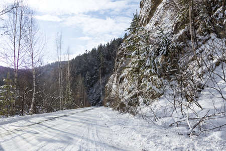 Snow-covered road and mountain slopes overgrown with forest in winter. Snowy road winter landscape