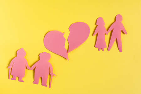 Colored cardboard figures of middle-aged and elderly people with a broken heart on a yellow...