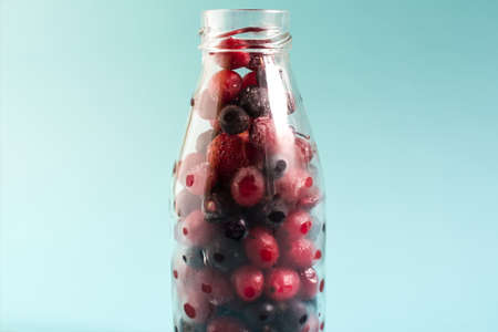 The concept of using quick-frozen products, a mixture of frozen berries in a transparent bottle on a...