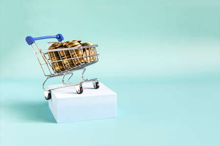 Metal basket on a blue podium filled with coins, light background business layout.の写真素材