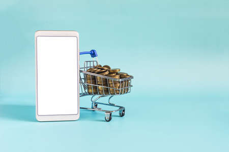 A metal basket filled with coins and a smartphone with a white screen on a light background online trading.の写真素材