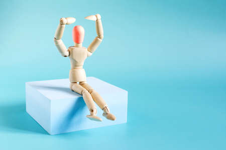 The figure of a wooden man on a blue podium with hands pointing to the head highlighted in red on a light background. The concept of diseases of the head.の写真素材