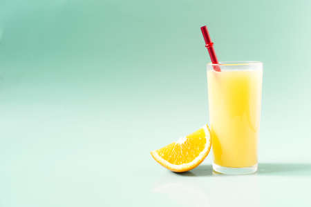 Natural orange juice in a transparent glass with a slice of orange and a bright red tube on a green background place for textの写真素材