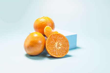 Tangerines and tangerine slices on a blue podium light blue background in natural light.