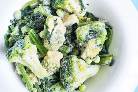 Frozen green vegetables with ice crystals on a light plate top viewの写真素材