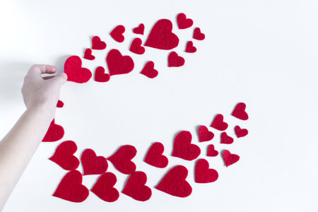 The hand lays out a red heart on a white background with large and small red hearts on a light background top view.の写真素材