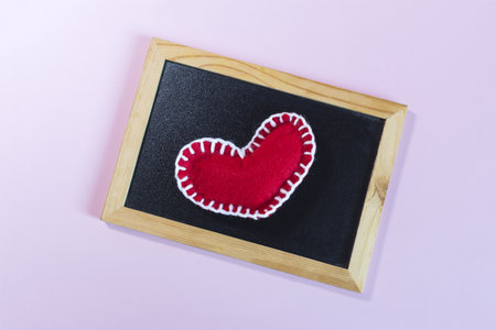 Wooden frame with a red heart embroidered with white threads on a light background.