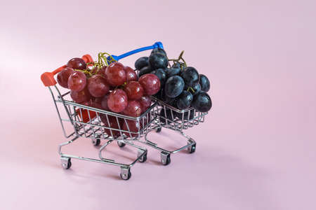 Red and black grapes in grocery baskets on a pink background.