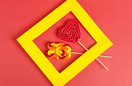 Two bright colored lollipops on sticks in a yellow frame on a bright red backgroundの写真素材