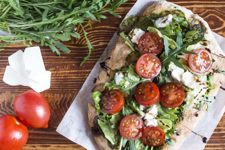 Fresh pinsa with cheese, tomatoes, cabbage and arugula on a natural wooden background top view.の写真素材