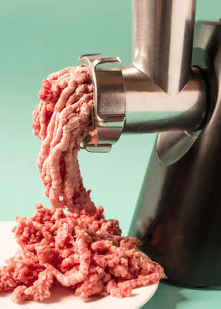 An electric meat grinder for households processes red meat on a light background.の写真素材