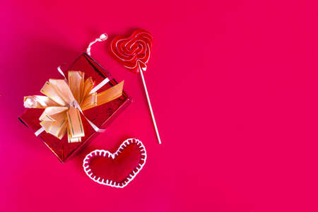 A bright background in red color scheme with a colored gift, a lollipop and a red heart flat lei.