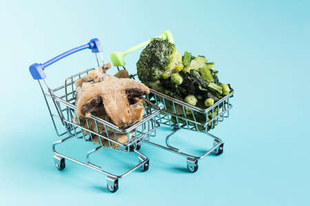 Frozen green vegetables and mushrooms champignons with ice crystals in metal carts on a light background of kopi spaceの写真素材
