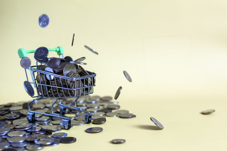 Coins of different sizes fall into a grocery basket filled to the brim with money on a yellow...