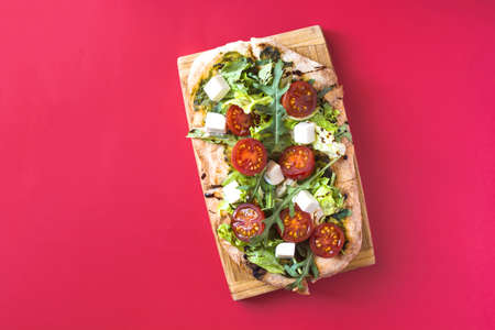 Homemade pizza with cheese, tomatoes, cabbage and arugula on a bright red background is a place for text.の写真素材