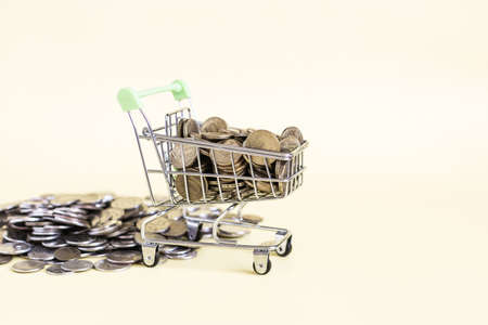 A grocery basket filled to the top with metal coins on a yellow background.