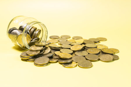 An overturned glass jar against the background of a scattering of yellow coins close-up.