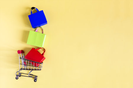 The concept of shopping and sales in retail. A metal basket and colored bags on a yellow background is a place for text.の写真素材