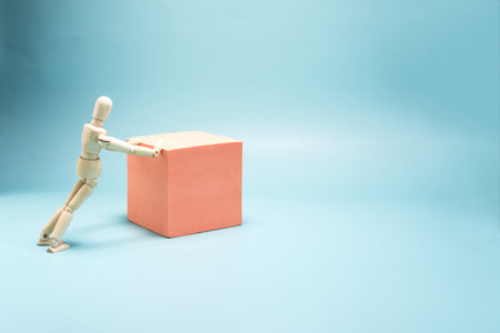 Abstraction the figure of a wooden man makes an effort to move a colored cube .の写真素材