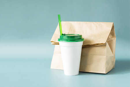 The concept of eating fast food, a paper bag with food for delivery and a plastic cup on a blue backgroundの写真素材