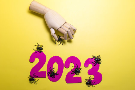 Abstract background with the numbers 2023, dark spiders and a wooden hand on a yellow background.
