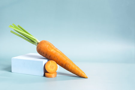 Fresh bright carrots and sliced carrots with a decor in the form of a blue podium on a blue background.の写真素材