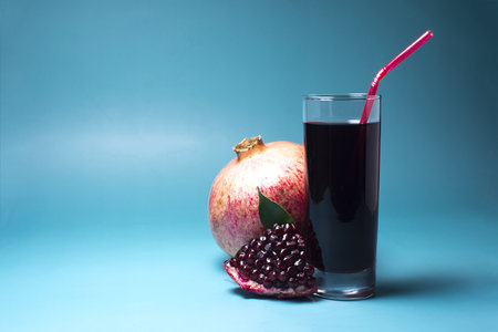 Pomegranate juice in a transparent glass with a red tube and a slice of pomegranate close-up on a light background.の写真素材