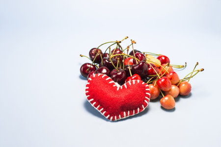 Two varieties of red and burgundy cherries with a red decorative heart on a blue background.の写真素材
