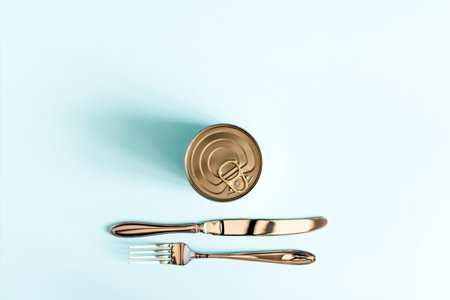 The concept of using canned food is a tin can and a fork and knife lying next to itの写真素材