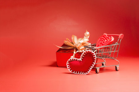 A bright background in a red color scheme with a shopping cart, a gift in a beautiful package and a red heart.の写真素材
