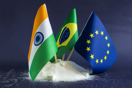 A mountain of granulated sugar and the flags of India, Brazil and the European Union in close-up on a dark background.の写真素材