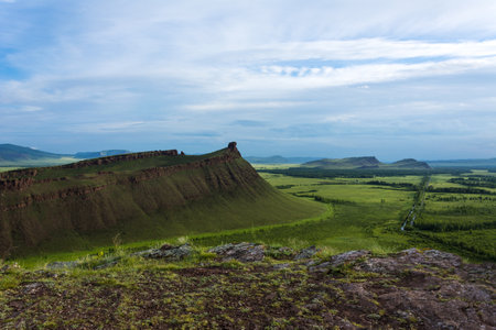 A rock on top of a green hill against a blue sky with cloudsの写真素材