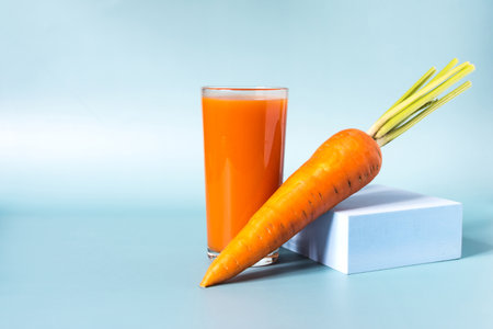 Fresh carrot juice in a transparent glass and fresh large carrots in close-up on a light backgroundの写真素材