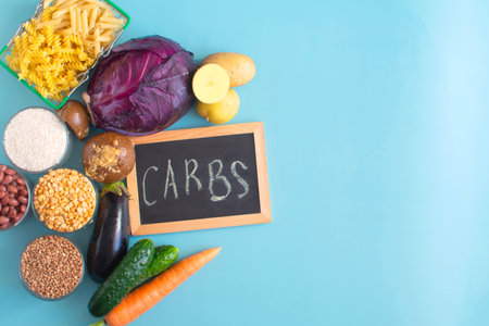 Foods containing complex carbohydrates in their composition, and the chalk inscription "carbohydrates" on a dark board is a place for textの写真素材