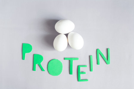Three large chicken eggs and the inscription in colored letters "protein" on a light backgroundの写真素材
