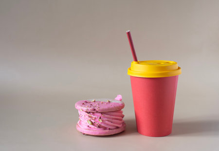 A sweet cake in pink colors and a red paper cup with a straw on a light background