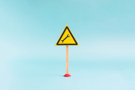 The "wrench" warning sign in a yellow triangle on the support, close-up on a blue background. The concept of a warning sign about a production, factory or factoryの写真素材