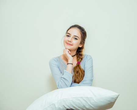 beautiful sleepy young woman with a pillow on the bed at homeの写真素材